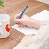 ノートにペンで文章を書く手元のイメージ